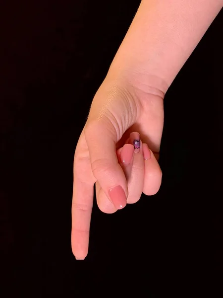 Sign hand, index finger points to the side, on a black background. A gesture with one finger, a pointer to the path. Female hand with forefinger.