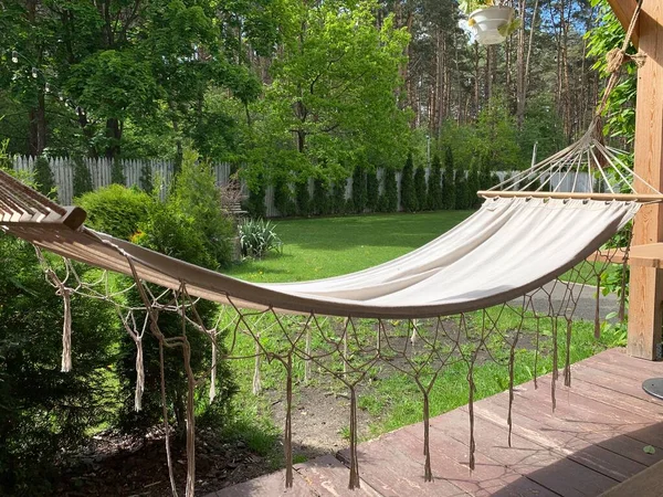 Empty hammock to relax on the terrace of the house. A hammock hangs in the yard in a green garden. Concept: outdoor recreation, weekend in the park