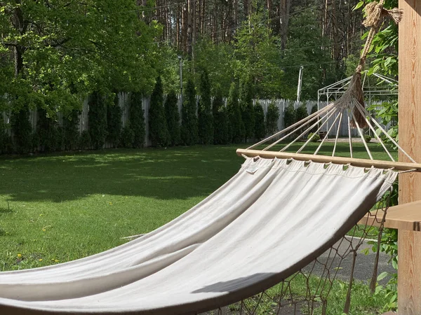 Empty hammock to relax on the terrace of the house. A hammock hangs in the yard in a green garden. Concept: outdoor recreation, weekend in the park