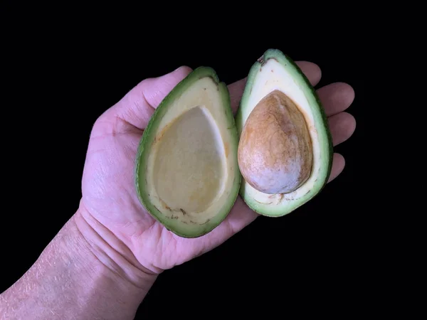 Halbierte Avocado Mit Einem Knochen Der Hand Auf Schwarzem Hintergrund — Stockfoto