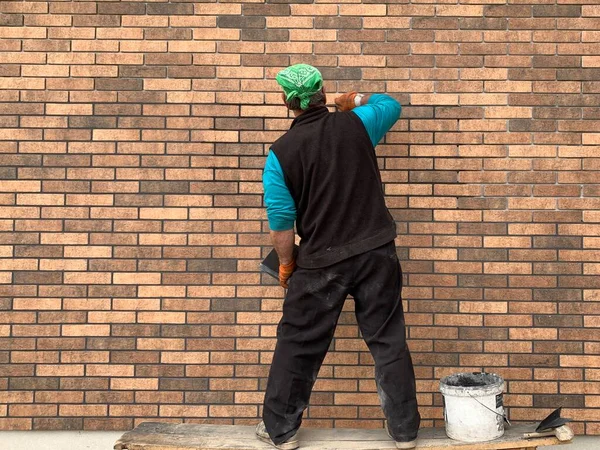 The master tiled the facade of the house. The builder closes the seams in the brickwork. Decorating the building with modern materials. — Stock Image Master Tiled Facade House Builder Closes Seams Brickwork Decorating Building Royalty Free Stock Photos