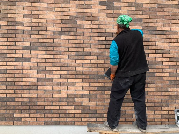 The master tiled the facade of the house. The builder closes the seams in the brickwork. Decorating the building with modern materials. — Stock Image Master Tiled Facade House Builder Closes Seams Brickwork Decorating Building Royalty Free Stock Images