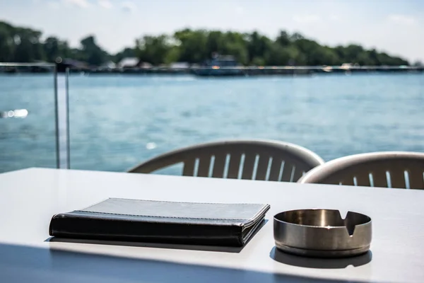 Notebook and ashtray on a table with lake in background