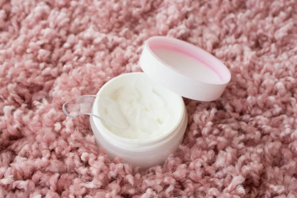 Wrinkle cream in a white jar on a pink fluffy bedspread. home skin care for the face and body.