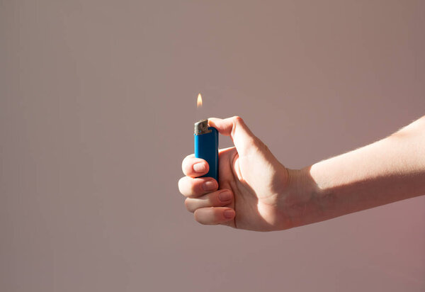 Lighter burns in the hand in the shade. A man holds a lighter with a flame. Fire and smoking concept