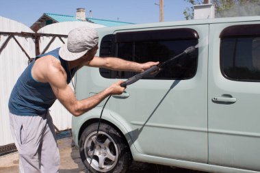 Delikanlı evin avlusunda su basıncıyla arabayı yıkıyor..