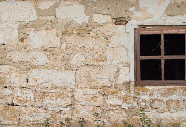 Wall of old blocks with a damaged wooden window without glass. Vintage village building.