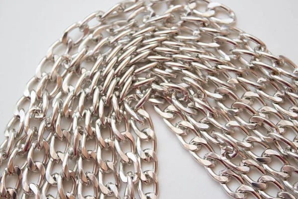 Metal chain closeup as a background, links of a silver chain on a white table, top view.