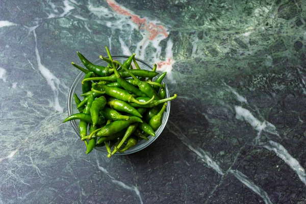 Fresh harvested green chili in a glass bowl on green marble texture background.Top view.