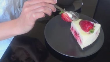 Bir kadın kremalı meyveli pasta, kek ve siyah cam bir masada bir fincan sade kahve yer.