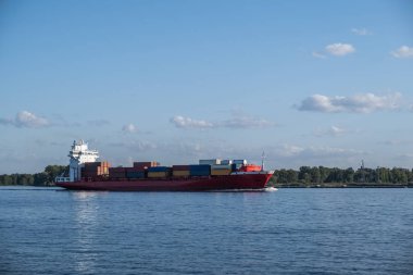 Güneşli bir günde seyir edebilen bir nehirde yelken açan bir kargo gemisi. Ortak.