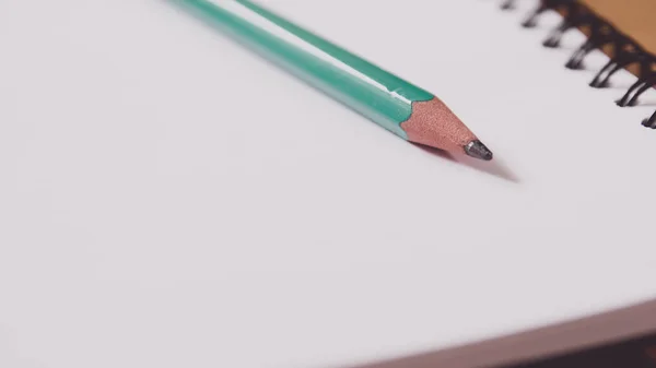 ノートに緑の鉛筆を閉める メモ帳はテーブルの上の空白のページで開きます — ストック写真