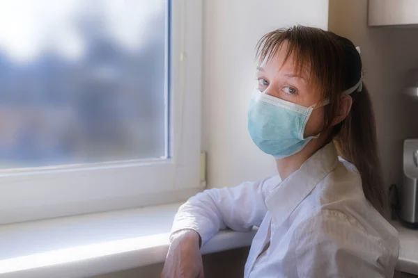 Sad girl wears mask sitting at home during quarantine and looking at camera. Stay home stay safe to prevent virus epidemic.