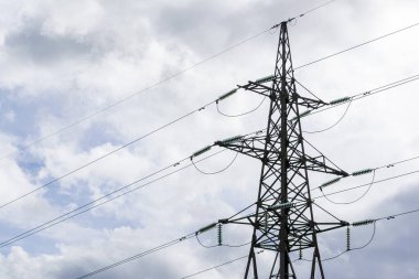Metal bir yüksek voltajlı güç iletim kulesi ve beyaz bulutlu mavi gökyüzüne karşı hatlar..