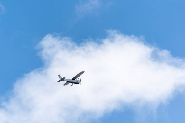 Single piston gray aircraft. Single-propeller aircraft flies over the blue sky against on white cloud.