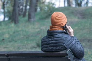 Şehir parkında bankta oturan bir adam cep telefonuyla konuşuyor..