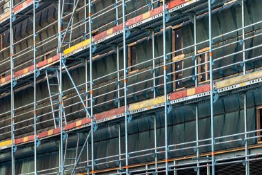 Metal iskelelerle inşaat halindeki binanın perspektifi, onarım alanının inşaatı.