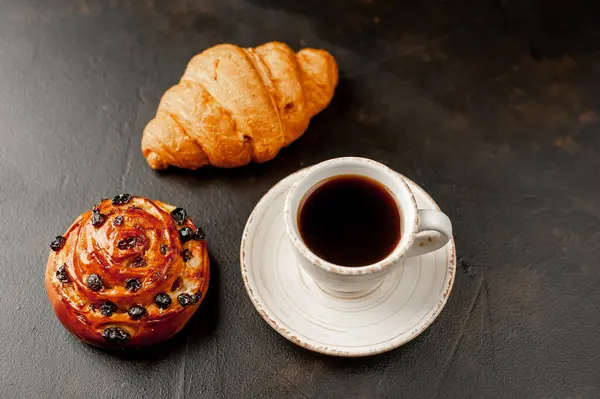 cup and coffee with bakery product on a dark background