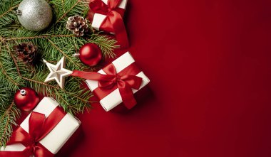 Kırmızı arka planda fiyonklu beyaz hediye kutuları, köknar dalları, toplar ve çam kozalakları.