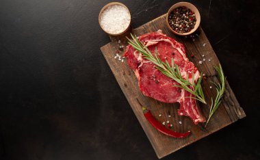 Tuzlu, biberiyeli çiğ biftek, ahşap tahtada siyah taş arka planda.