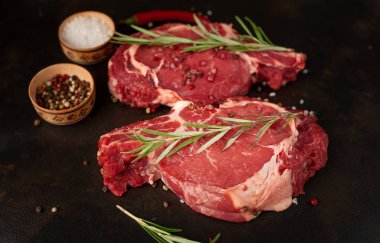 Siyah taş arka planda tuzlu, biberiyeli çiğ biftek.
