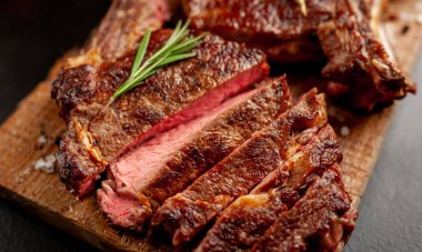 Dilimlenmiş biftekler tahtanın üzerinde, siyah taş arka planda.