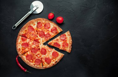 Siyah arka planda pizza kesicili dilimlenmiş pepperoni pizza.
