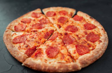 Siyah arka planda dilimlenmiş pepperoni pizza.