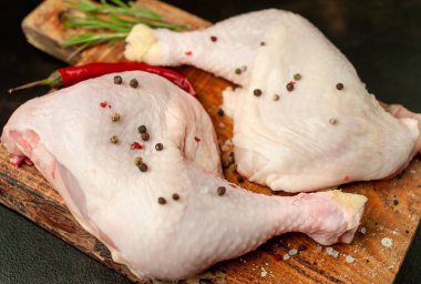 Çiğ tavuk budu, ahşap tahtada baharatlar, siyah taş arka planda.