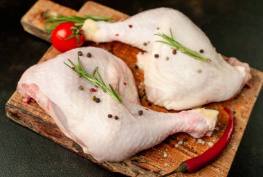 Çiğ tavuk budu, ahşap tahtada baharatlar, siyah taş arka planda.