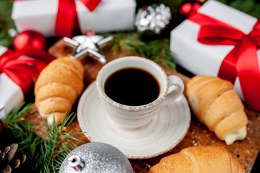 Ahşap tahtada servis edilen sıcak kahve ve şenlikli kış arkaplanda kruvasanlar.