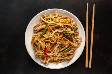 Siyah taş zemin üzerinde çubuklarla servis edilen baharatlı Asya makarnası.