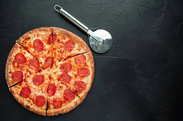 Sliced pepperoni pizza with pizza cutter on black background