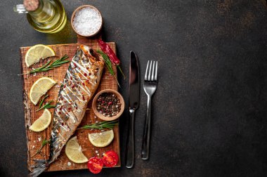 Tahtada servis edilen limonlu, domatesli ve biberiyeli fırında uskumru.