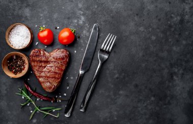 Etli biftek, çatal bıçak ve domates.