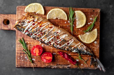 Tahtada servis edilen limonlu, domatesli ve biberiyeli fırında uskumru.