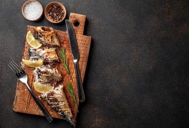 Tahtada servis edilen limonlu ve çatal bıçaklı fırında uskumru.