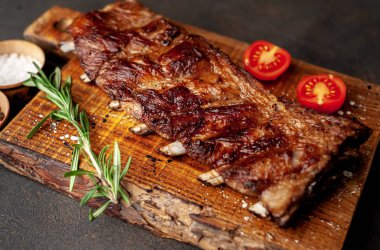 Ahşap tahtada kızarmış domuz pirzolası, baharat, biberiye ve domates.