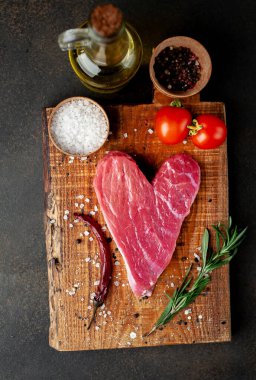 Ahşap tahtada baharat ve sebzeli çiğ kalp şeklinde et. Sevgililer Günü konsepti.