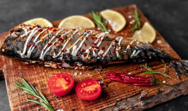 Tahtada servis edilen limonlu, domatesli ve biberiyeli fırında uskumru.