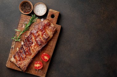Ahşap tahtada kızarmış domuz pirzolası, baharat, biberiye ve domates.