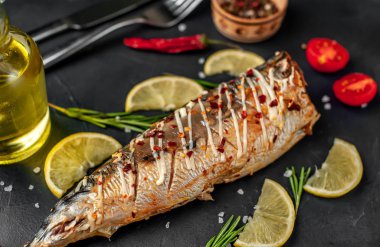 Limonlu fırında uskumru, domates ve çatal ve bıçakla servis edilen biberiye.