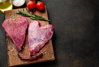 Ahşap tahtada baharatlı, yağlı ve domatesli çiğ biftek. Sevgililer Günü konsepti.