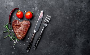 Etli biftek, çatal bıçak ve domates.