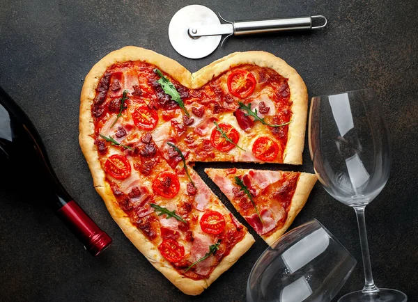 Pizza in heart shape with cutter, wine glasses, bottle.