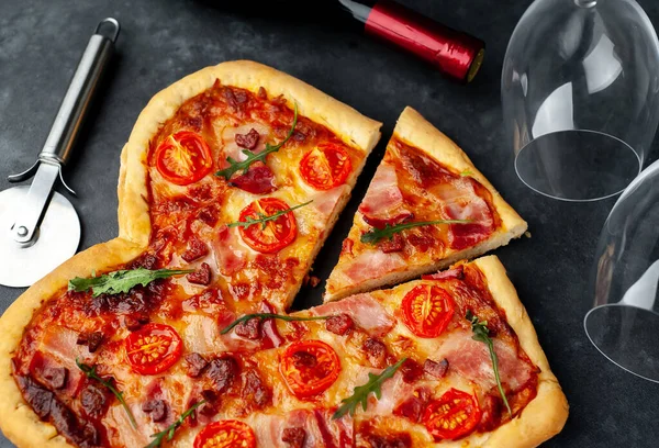 Pizza in heart shape with cutter, wine glasses, bottle.