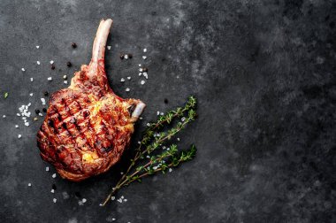 steak - grilled beef tomahawk with spices, thyme on a stone background