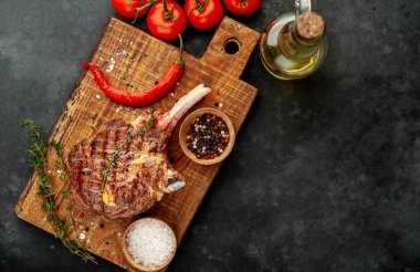 grilled beef steaks - tomahawk with tomatoes and red pepper on a stone background
