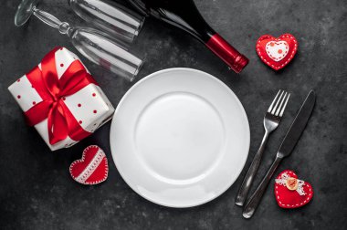 Table setting for Valentine's Day - white plate, wine, gift, kitchen appliances, hearts on a stone backgroundA