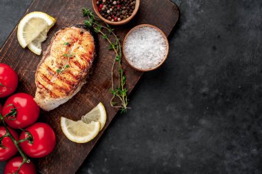 Grilled salmon steak with spices, lemon and tomatoes on a stone background.